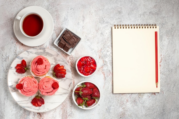 Draufsicht von rosa Erdbeerkuchen mit Sahne und Tasse Tee auf weißer Oberfläche