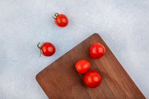 Draufsicht von roten frischen und Kirschtomaten auf einem hölzernen Küchenbrett auf weißer Oberfläche