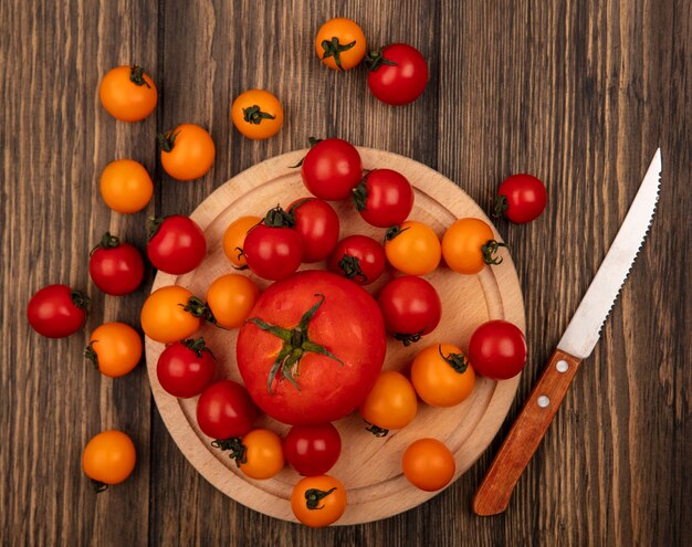 Draufsicht von roten Tomaten auf einem hölzernen Küchenbrett mit Messer mit Kirschtomaten lokalisiert auf einer hölzernen Oberfläche