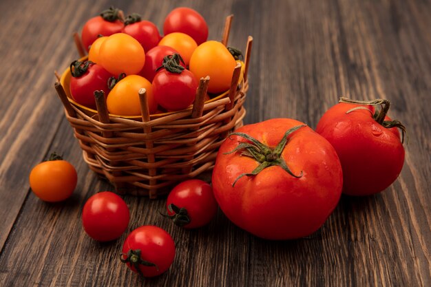 Draufsicht von roten und orange Kirschtomaten auf einem Eimer mit großen weichen Tomaten lokalisiert auf einer Holzoberfläche