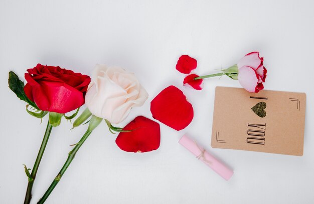 Draufsicht von roten und weißen Rosen mit kleiner Postkarte auf weißem Hintergrund