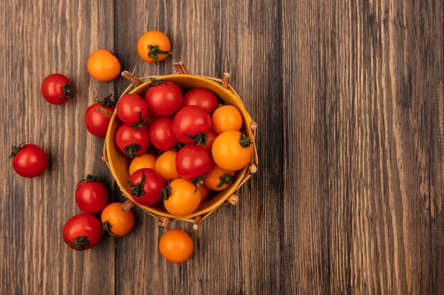 Draufsicht von saftigen roten und orange Kirschtomaten auf einem Eimer mit Tomaten lokalisiert auf einer Holzwand mit Kopienraum