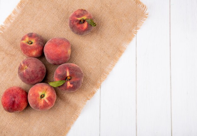 Draufsicht von saftigen und frischen Pfirsichen auf Sackleinen auf weißer Oberfläche