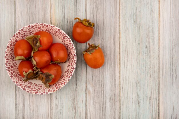 Draufsicht von saftigen weichen Kakis auf einer Schüssel mit Kakis lokalisiert auf einer grauen Holzwand mit Kopierraum