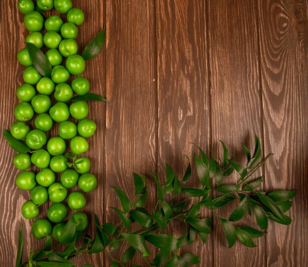 Draufsicht von sauren grünen Pflaumen mit Ruscusblättern auf Holztisch mit Kopienraum