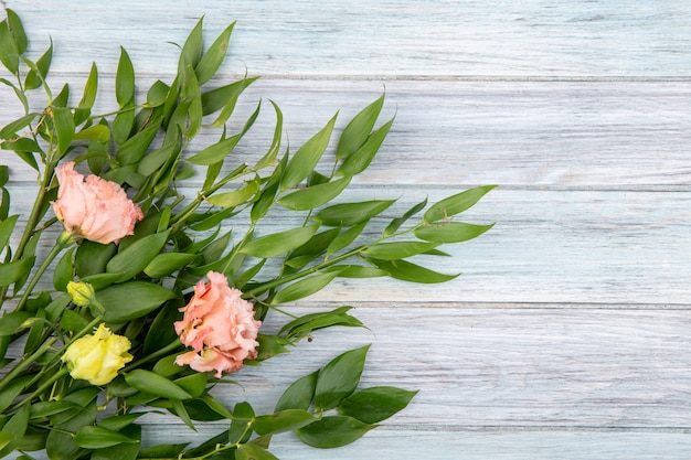 Draufsicht von schönen Blumen wie rosa Pfingstrosen und gelben Rosen mit grünen Blättern auf Holz mit Kopienraum