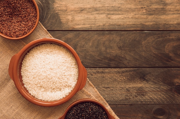 Draufsicht von Schwarz; Rote und weiße organische Reiskörner auf Jutefasertuch über dem Holztisch