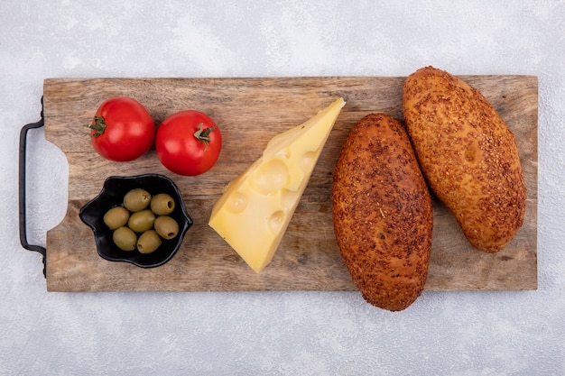 Draufsicht von Sesamfrikadellen auf einem hölzernen Küchenbrett mit grünen Oliven auf einer schwarzen Schüssel mit Tomaten und Käse auf einem weißen Hintergrund