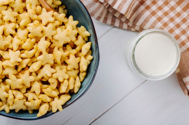 Draufsicht von sternförmigen Cornflakes in einer Schüssel und einem Glas Milch auf dem weißen Holztisch