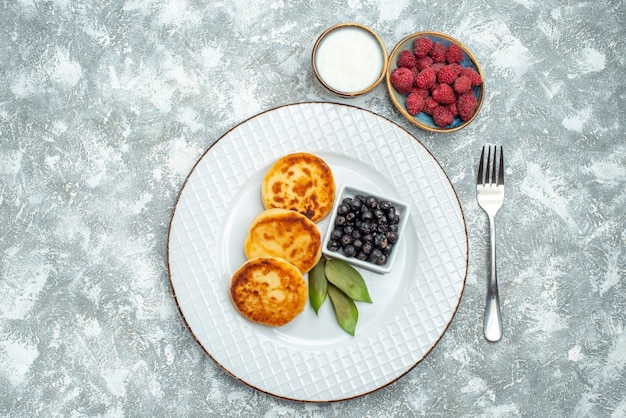 Draufsicht von süßen Muffins mit Beeren innerhalb Platte auf der hellen Oberfläche