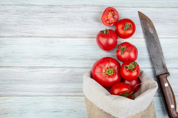 Draufsicht von Tomaten, die aus Sack und Messer auf Holzoberfläche mit Kopierraum verschüttet werden