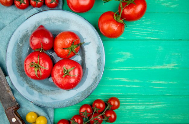 Draufsicht von Tomaten in Platte mit anderen und Messer auf Stoff und grüner Oberfläche mit Kopierraum