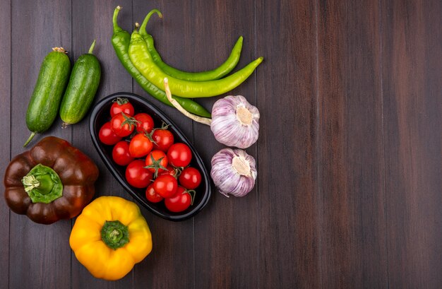 Draufsicht von Tomaten in Schüssel und Gurken-Knoblauchpfeffer herum auf Holzoberfläche