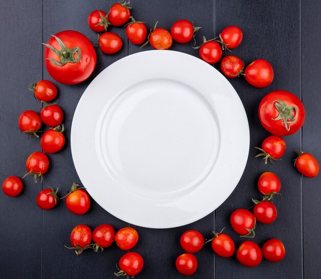 Draufsicht von Tomaten um leere Platte auf schwarzer Oberfläche