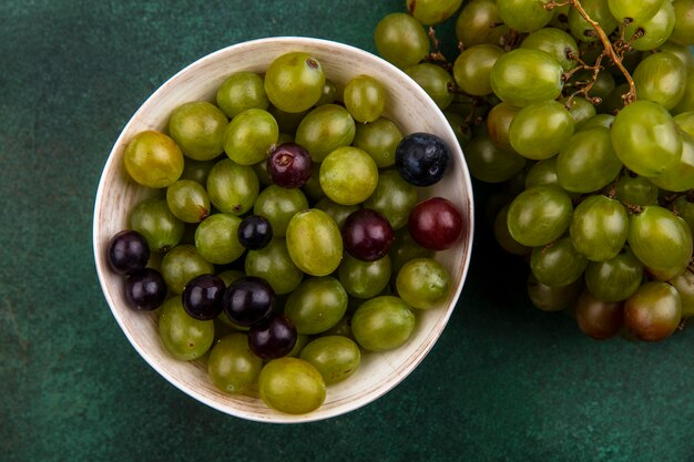 Draufsicht von Traubenbeeren in Schüssel und Weintraube auf grünem Hintergrund