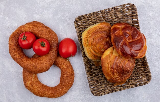 Draufsicht von türkischen Sesambagels mit frischen Tomaten und einem Eimer Brötchen auf einem weißen Hintergrund