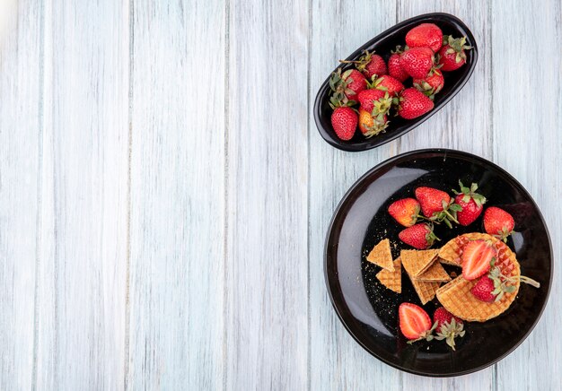 Draufsicht von Waffelkeksen mit Erdbeeren in Tellern auf Holzoberfläche