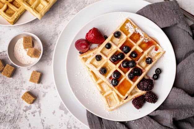 Draufsicht von Waffeln auf Platte mit Zusammenstellung von Früchten und von Zuckerwürfeln