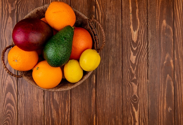 Draufsicht von Zitrusfrüchten als Mangoorange Avocado-Zitrone im Korb auf der linken Seite und hölzernem Hintergrund mit Kopienraum