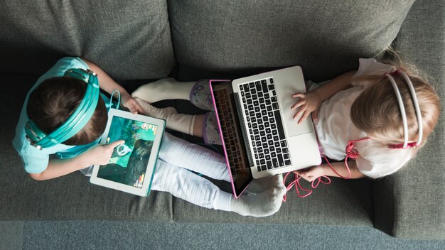 Draufsicht von zwei Kindern mit Laptop und Tablette