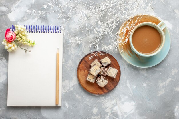 Draufsicht Waffeln mit Notizblock und Milchkaffee auf dem grauweißen Schreibtisch Schokoladenkeks trinken Kaffee