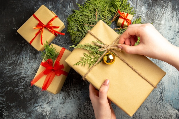 Draufsicht Weihnachtsgeschenk in weiblicher Hand kleine Geschenke Tannenzweige auf grauer Oberfläche