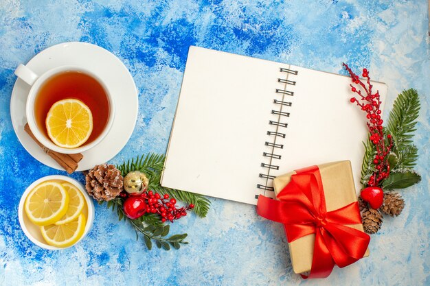 Draufsicht Weihnachtsgeschenk mit rotem Band auf Notebook-Weihnachtsbaum-Zweig gebunden eine Tasse Tee auf blauem Tisch