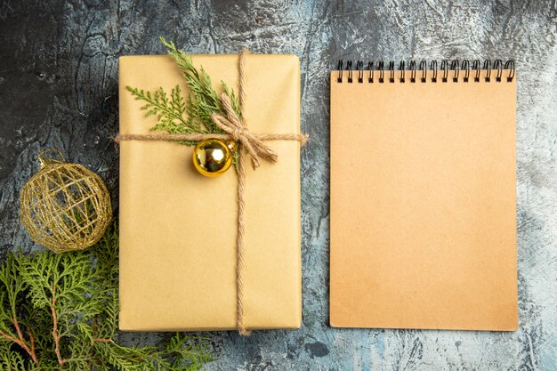Draufsicht Weihnachtsgeschenk Tannenzweige Weihnachtskugel Notizbuch auf grauer Oberfläche