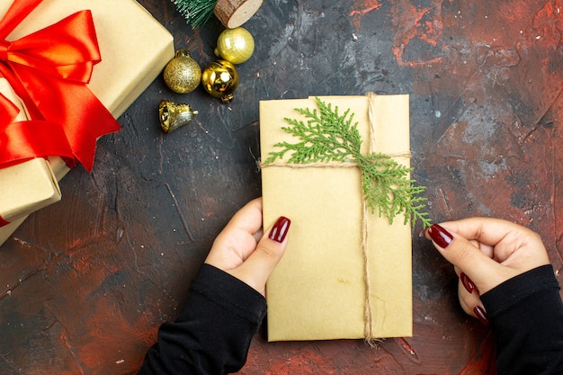 Kostenloses Foto draufsicht weihnachtsgeschenke goldene weihnachtskugeln geschenk in frauenhänden auf dunkelrotem tisch