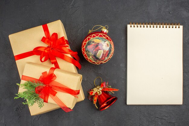 Draufsicht Weihnachtsgeschenke in braunem Papier mit rotem Band Weihnachtsbaum Spielzeug Notizblock auf dunkler Oberfläche gebunden