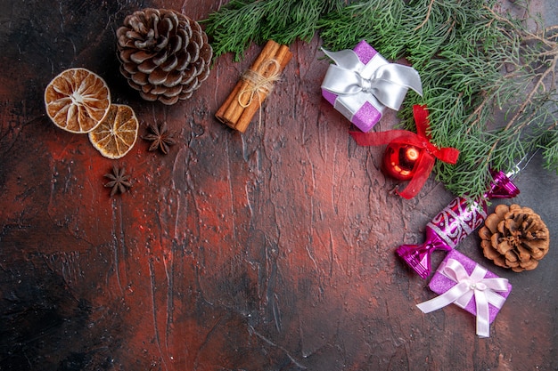 Draufsicht Weihnachtsgeschenke Kiefernzweige mit Kegel Weihnachtsbaum Spielzeug Zimt getrocknete Zitronenscheiben Anis auf dunkelroter Oberfläche