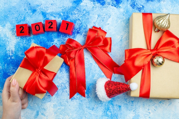 Draufsicht weihnachtsgeschenke kleine weihnachtsmütze holzblöcke rote schleife geschenk in weiblicher hand auf blauweißem tisch
