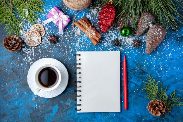 Draufsicht Weihnachtsgeschenke Tannenbaum Zweige Kegel Anis Notizbuch eine Tasse Tee auf blauem Hintergrund freier Platz