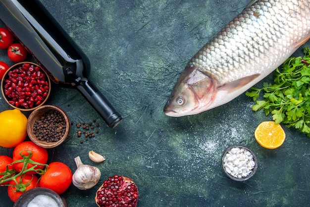 Draufsicht Weinflasche roher Fisch Tomaten Knoblauch grün Granatapfel verschiedene Gewürze in kleinen Schüsseln auf dem Tisch