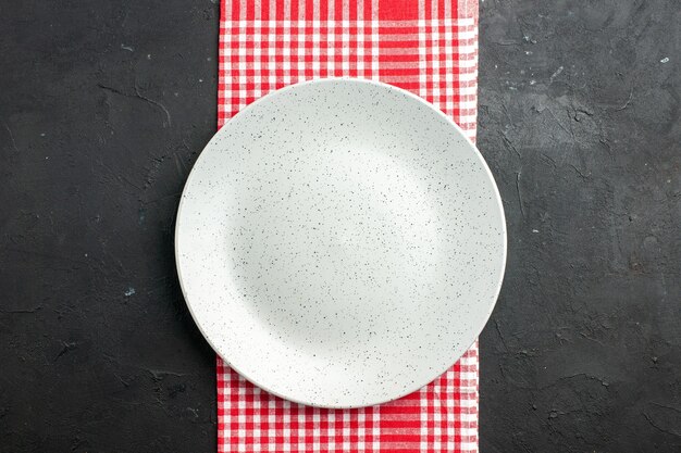 Draufsicht weiße runde Platte auf roter und weißer karierter Serviette auf dunklem Tischkopierplatz