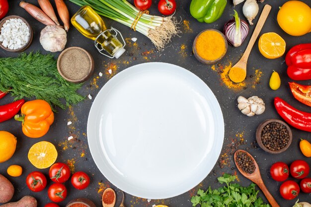 Draufsicht weißer runder Teller schwarzer Pfeffer Kurkuma und Meersalz in kleinen Schalen Knoblauchtomaten Koriander Dill Frühlingszwiebeln Ölflasche auf dem Tisch