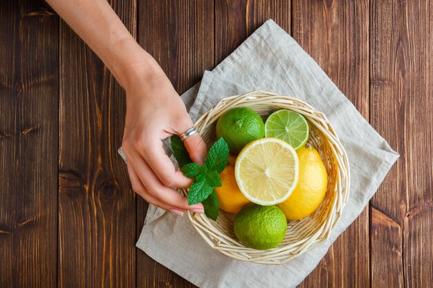 Draufsicht-Zitronen im Korb mit Hand, die Zitronenblätter auf Holzoberfläche hält.