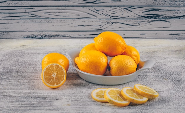 Draufsicht-Zitronen in Platte und mit Scheiben auf grauem hölzernem Hintergrund. horizontal