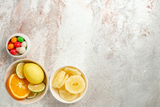 Draufsicht Zitrusfrüchte Schalen mit bunten Bonbons getrocknete Ananas und Zitrusfrüchte auf der linken Seite des Tisches