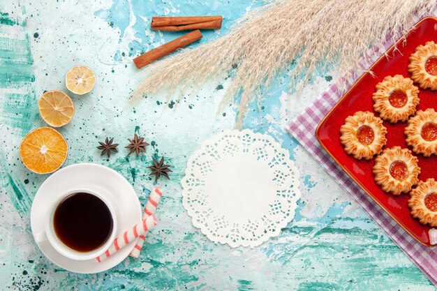 Draufsicht-Zuckerplätzchen innerhalb der roten Platte mit Tasse Tee auf dem blauen Hintergrund