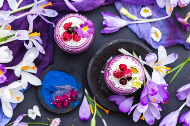 Draufsichtaufnahme einer schönen Anzeige der lila veganen Smoothies, die mit bunten Blumen geschmückt werden