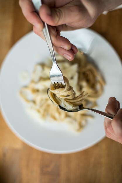 Draufsichtaufnahme eines Mannes, der köstliche Spaghetti auf einer Gabel wirbelt