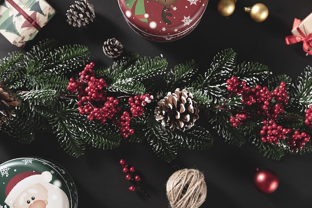 Draufsichtaufnahme von Tannenzweigen mit Kegel und Geschenk auf einem schwarzen Tisch - Konzept von Weihnachten