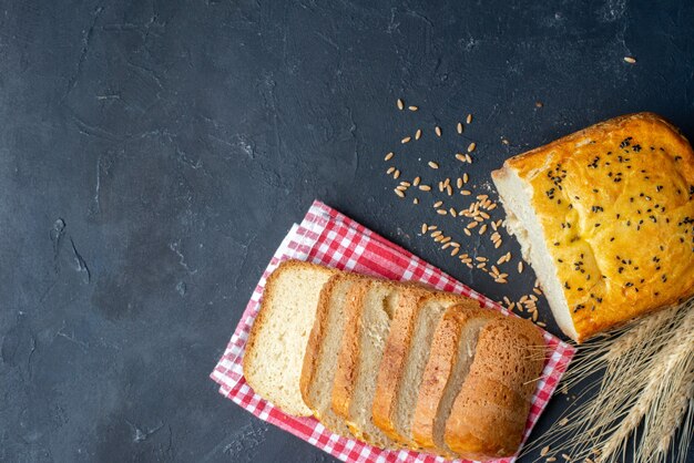 Draufsichtbrotscheiben auf rot-weiß kariertem Küchentuch Weizenspitzen und Körner auf dunklem Tischfreiraum