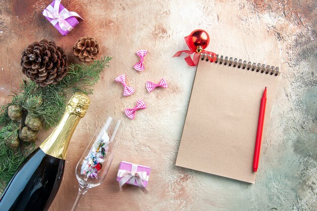 Draufsichtflasche Champagner mit kleinen Geschenken und Notizblock auf hellem Weihnachtsfoto Neujahrsgeschenk Alkohol