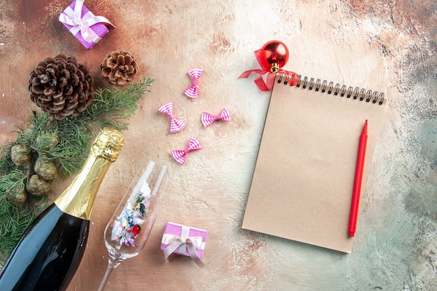 Draufsichtflasche Champagner mit kleinen Geschenken und Notizblock auf hellem Weihnachtsfoto Neujahrsgeschenk Alkohol