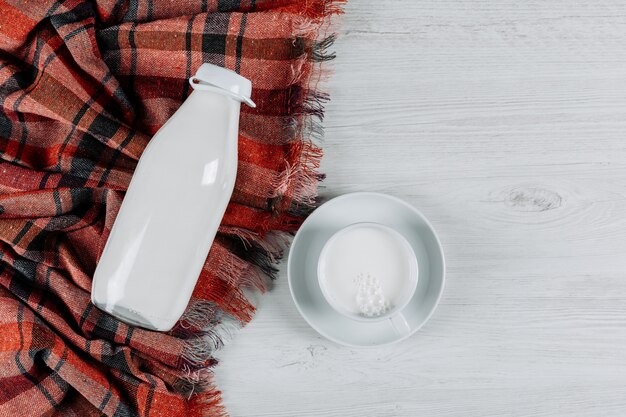 Draufsichtflasche Milch mit Tasse Milch auf weißem Holz- und Picknicktuchhintergrund. horizontal