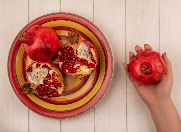 Draufsichtfrau, die Granatapfel in ihrer Hand und auf einem Teller auf einer weißen Wand hält