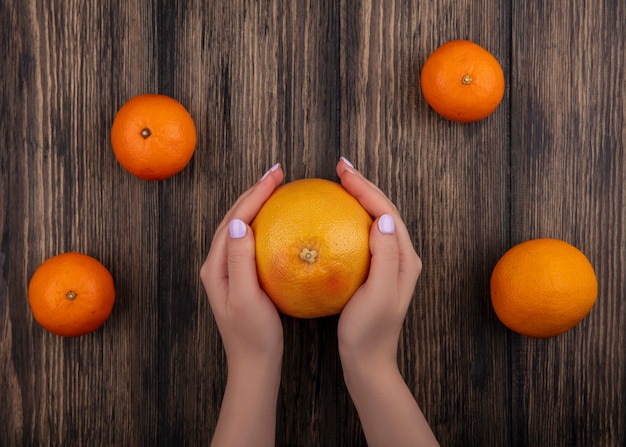 Draufsichtfrau, die Grapefruit mit Orangen auf hölzernem Hintergrund hält