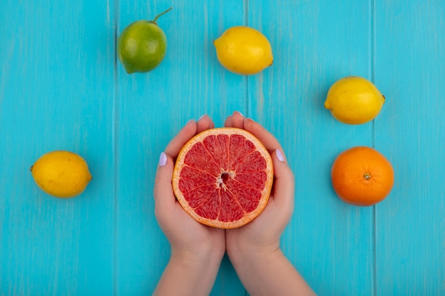 Draufsichtfrau, die halbe Grapefruit mit Limette und Zitronen auf türkisfarbenem Hintergrund hält